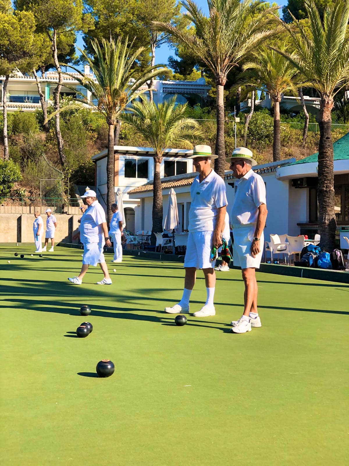 Players on the Miraflores Bowls Club green, with palm trees and Spanish villas in the background